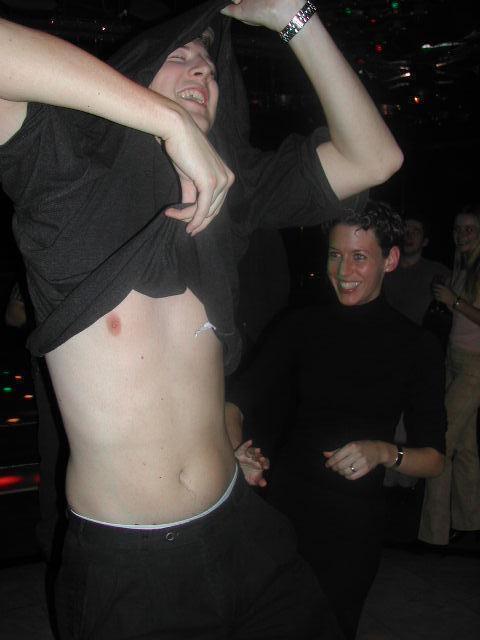 A man lifts his shirt while dancing, revealing his torso.