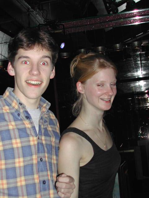 A young man with red-eye effect smiles widely while standing next to a woman who is also smiling.