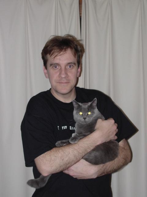 A man in a black shirt holds a gray cat in his arms, looking at the camera.