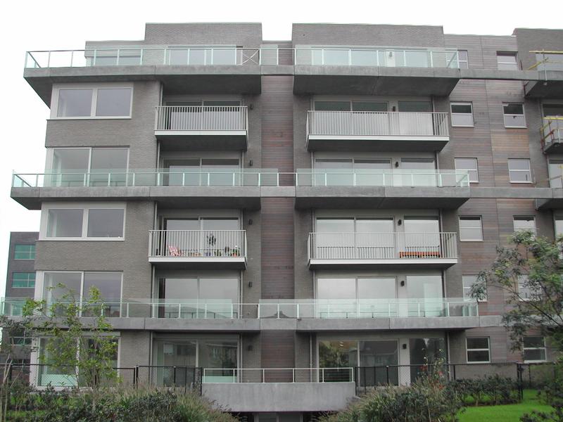 A modern apartment building with multiple balconies and large windows, surrounded by greenery.
