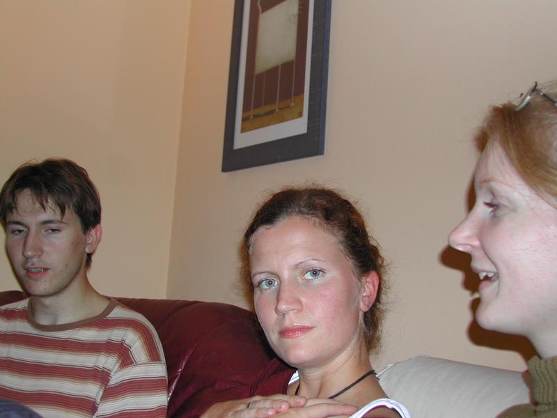 Three people sitting on a couch, one laughing while the others have neutral or unimpressed expressions.