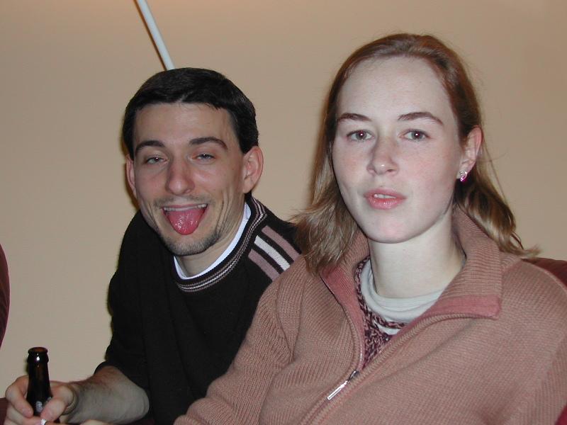 A man playfully sticks out his tongue while a woman sits beside him, looking at the camera.