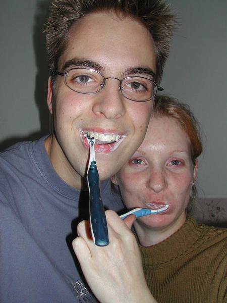 Two people brushing their teeth together, one brushing the other's teeth while smiling.