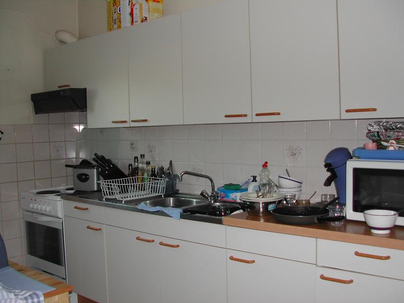 A kitchen with white cabinets, a stove, a sink, and countertops cluttered with dishes, utensils, and appliances.