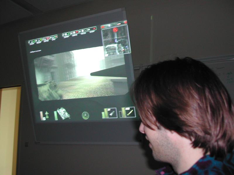 A person watches a projected screen displaying a first-person shooter video game during a LAN party.