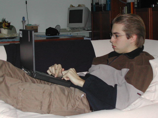 A person reclines on a sofa, typing on a laptop with a focused expression.