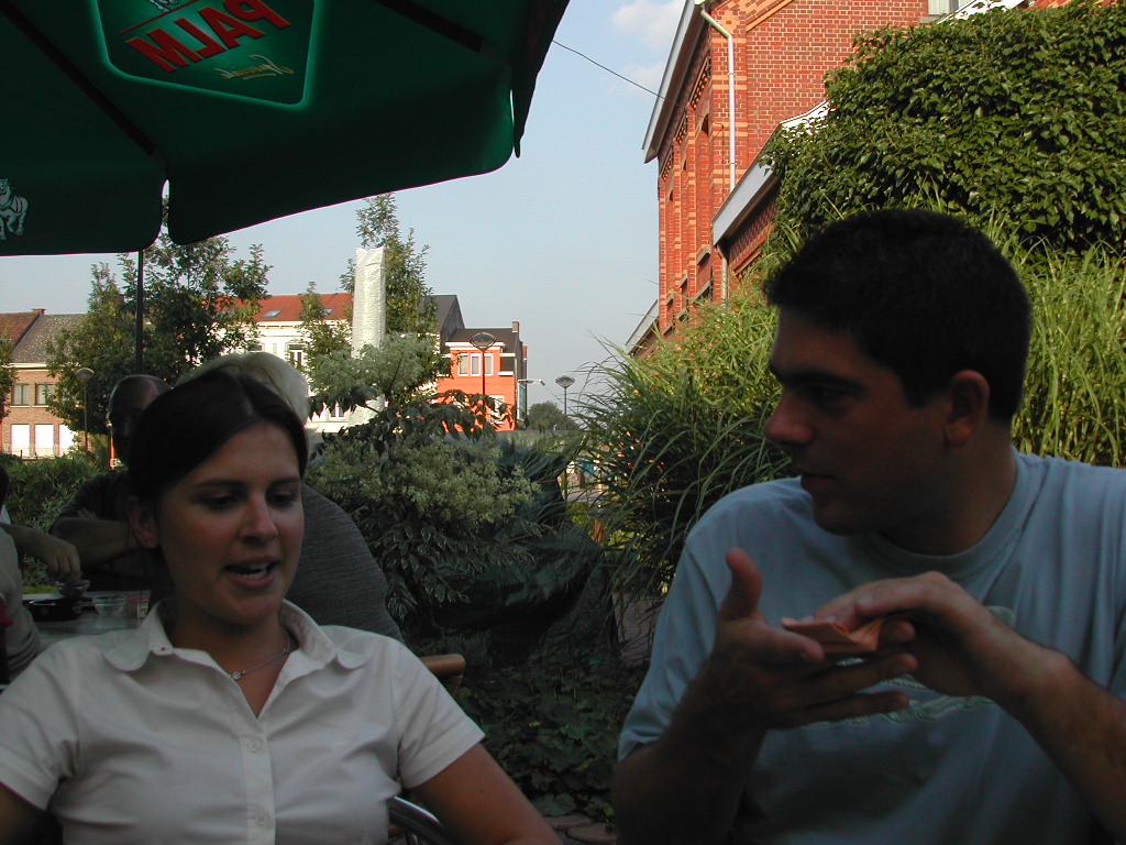 A woman and a man sit at an outdoor table, engaged in conversation.