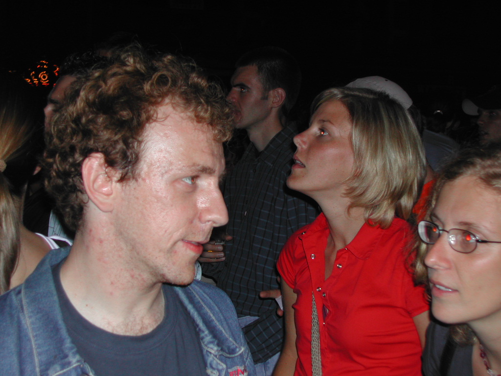 A group of people at a crowded event, with one woman speaking and others focused on something nearby.