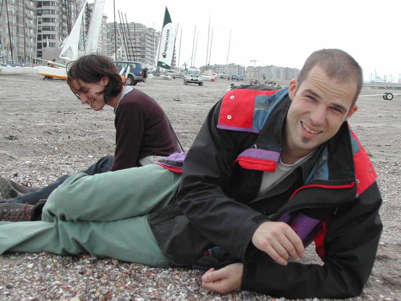 Two people sitting on a sandy beach, smiling and laughing.
