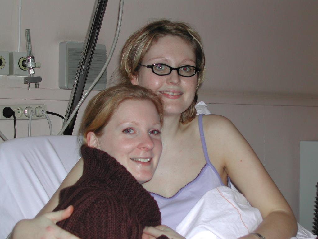 Two women sitting on a hospital bed, smiling and embracing each other.
