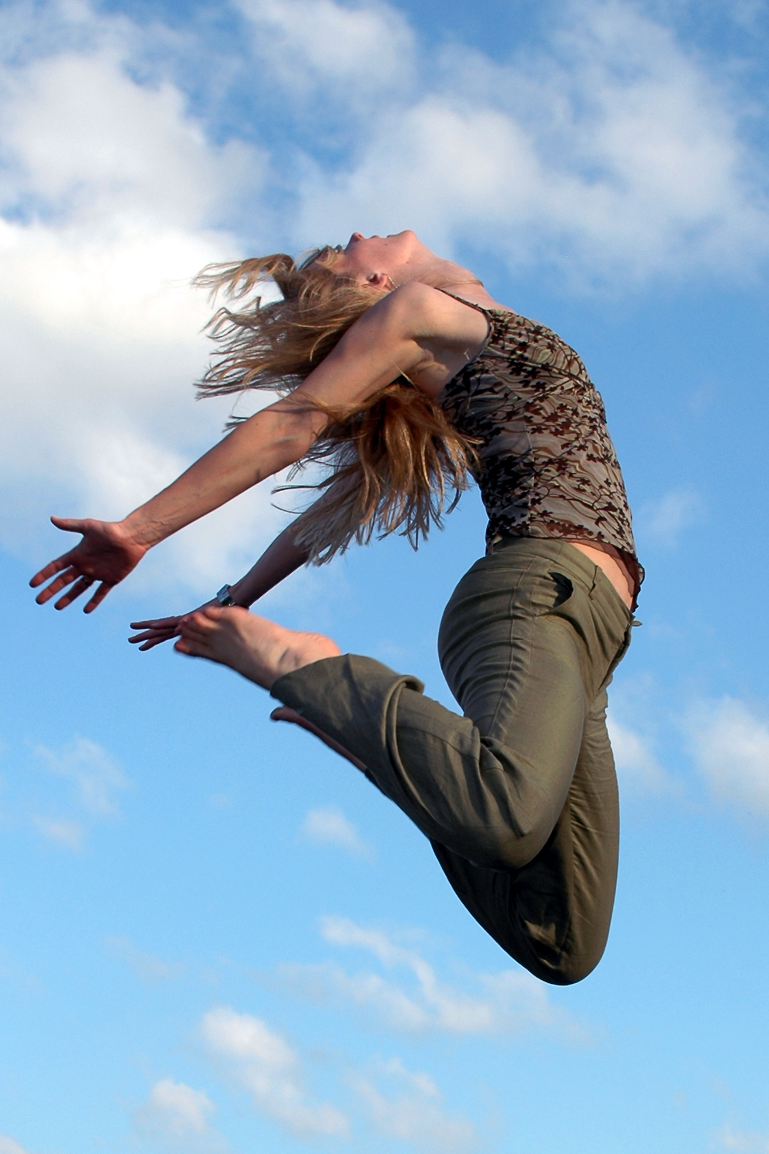 A person jumps in mid-air with arms and legs extended against a blue sky with scattered clouds.