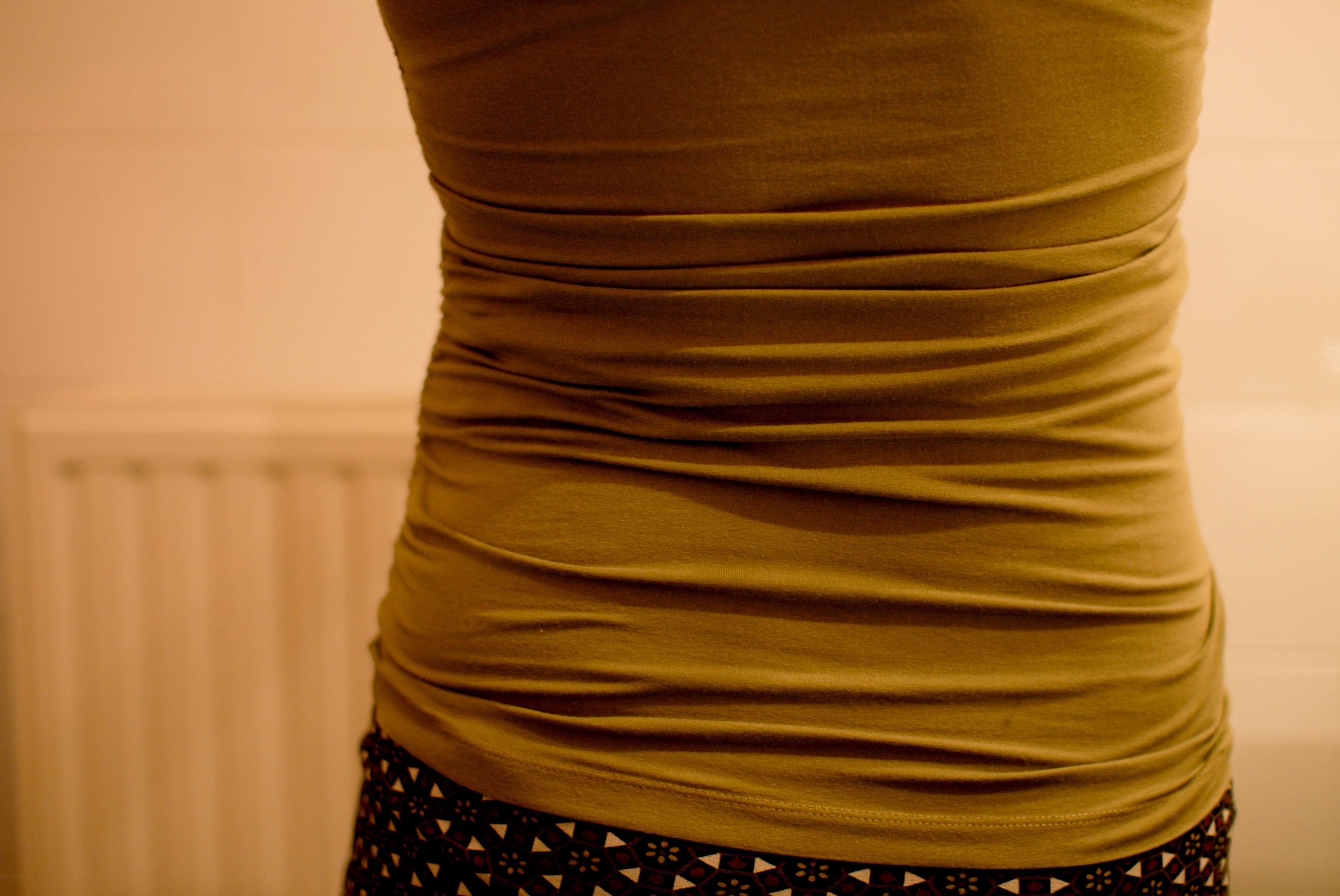 A close-up of a pregnant person's belly at 39 weeks, covered by a fitted olive-green shirt.