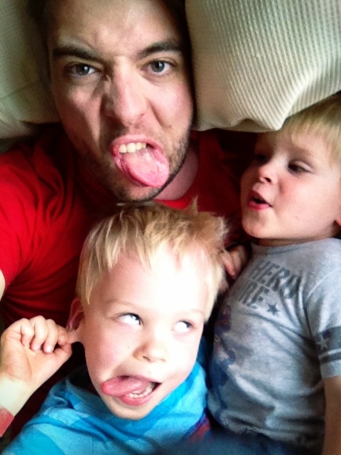 A man and two young children make silly faces while lying close together on a couch.
