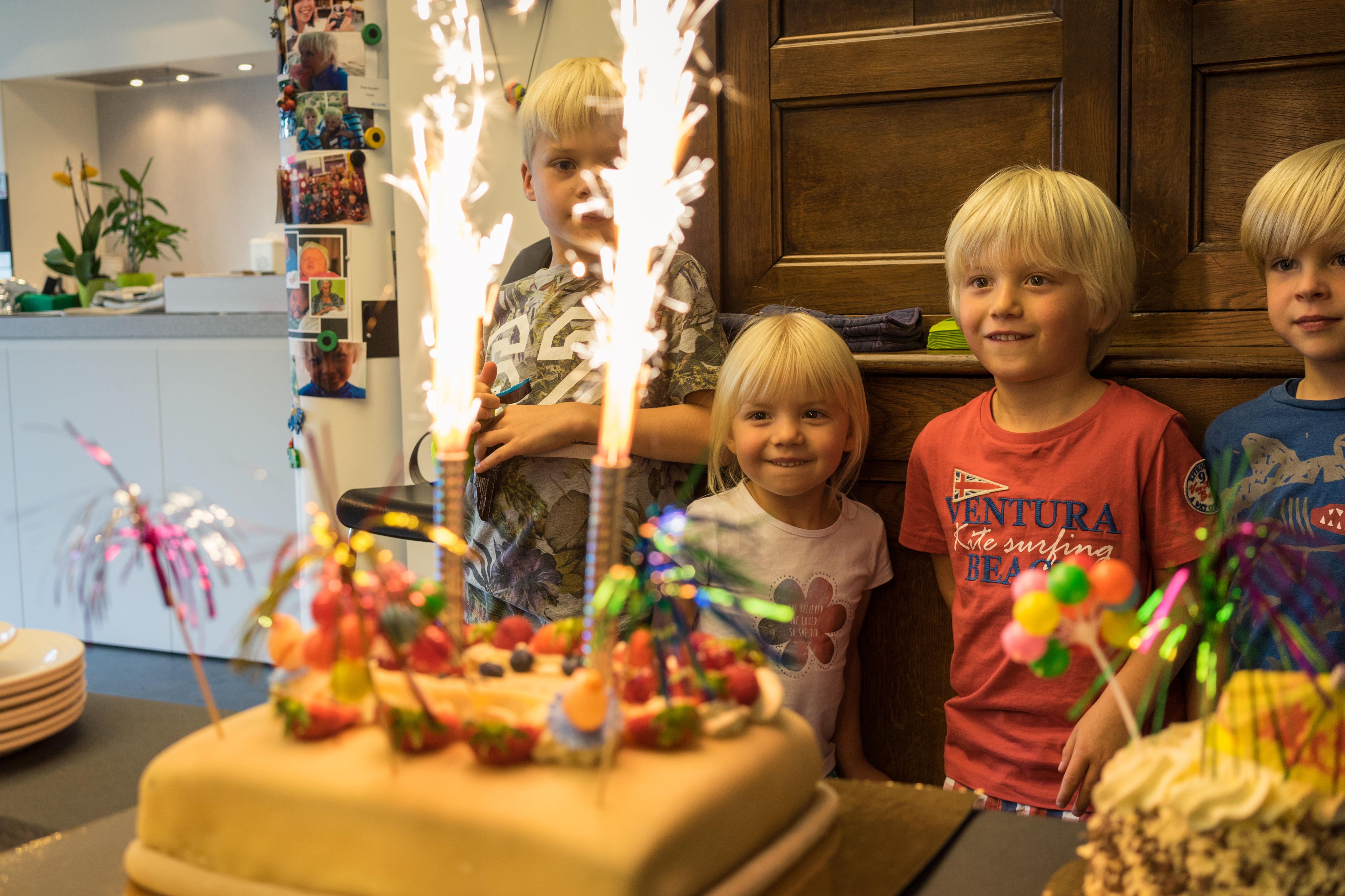 Children watch a cake with lit sparklers, smiling and excited.
