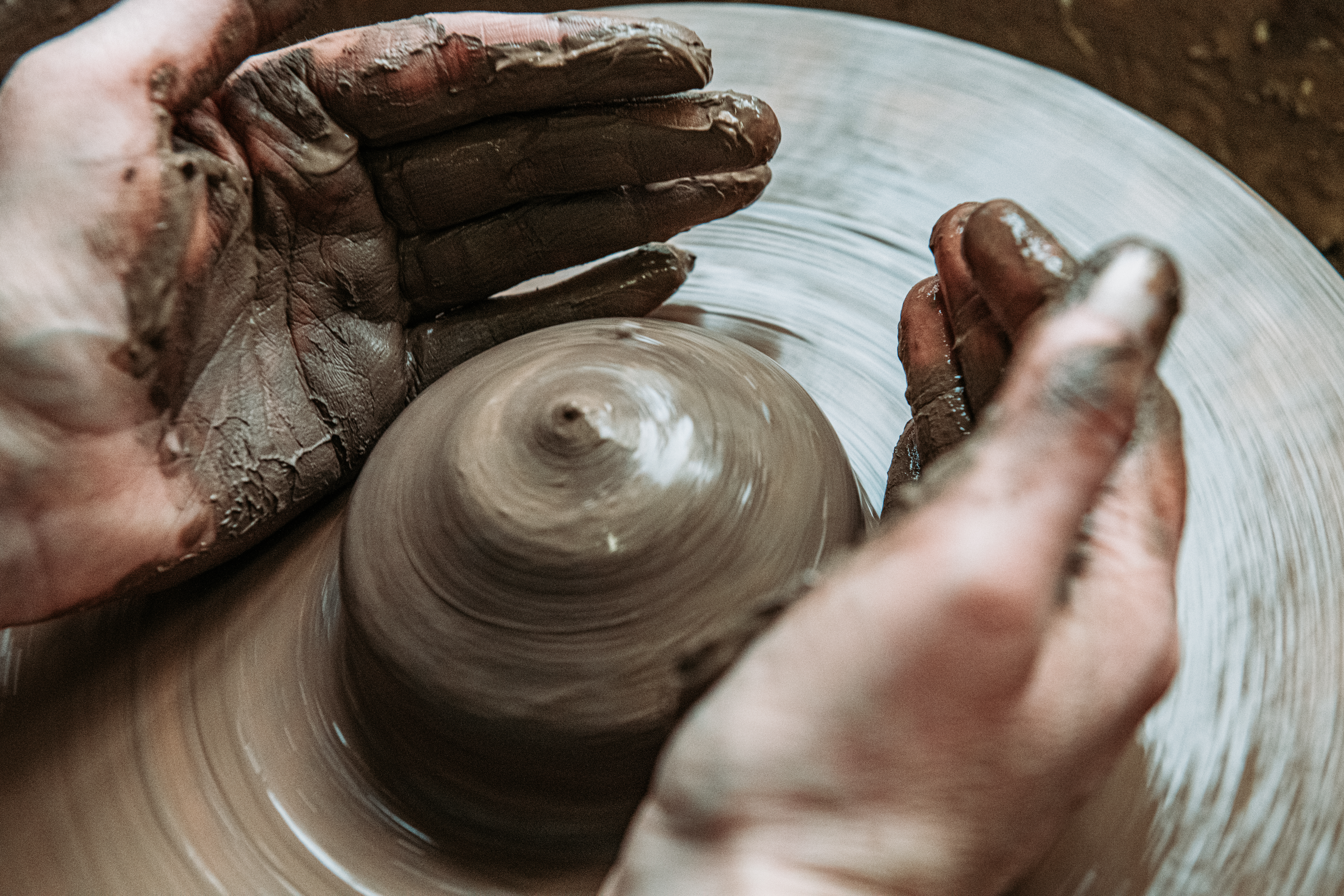Hands covered in wet clay shape a spinning pottery piece on a wheel.