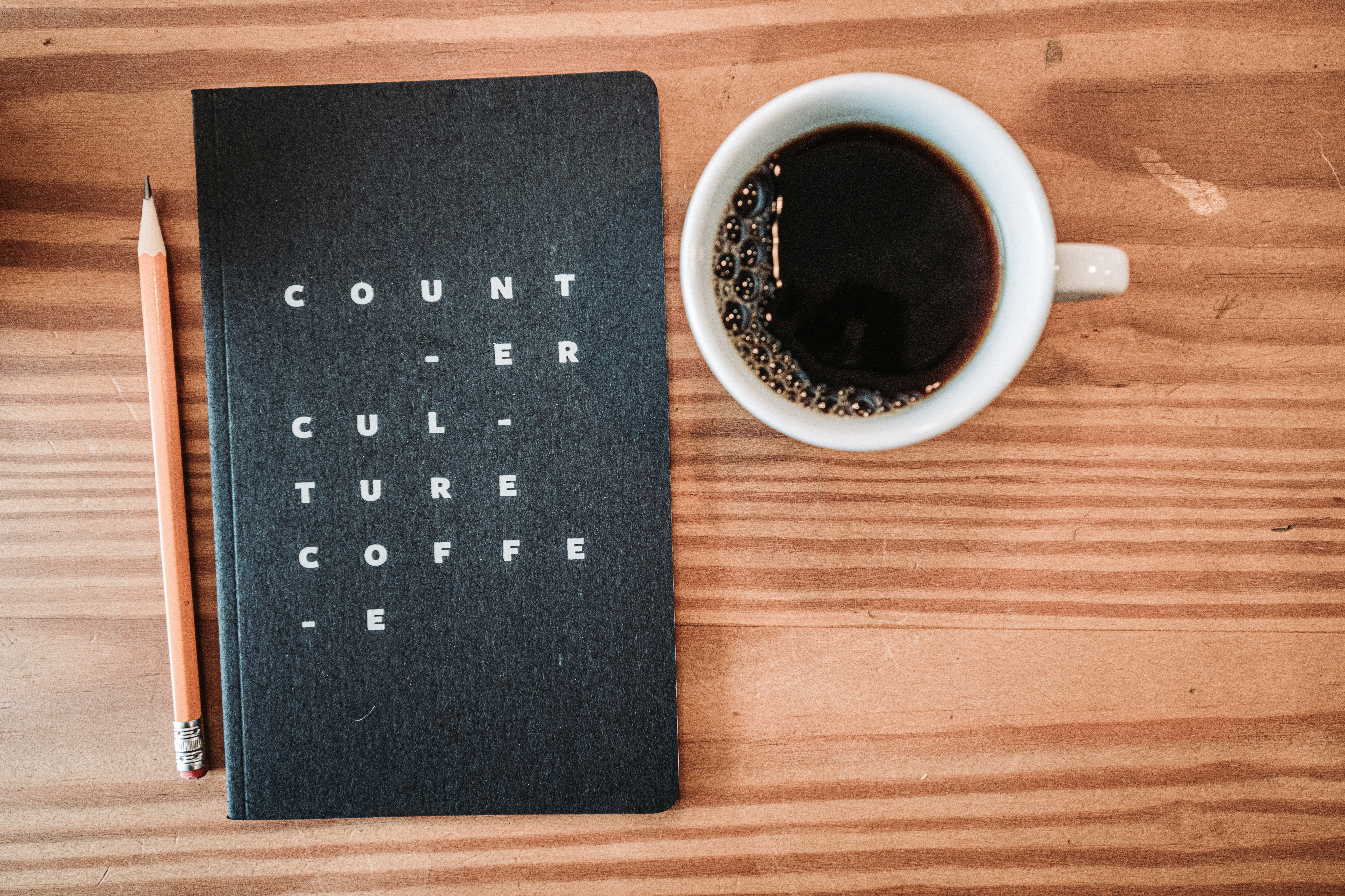 A notebook labeled "Counter Culture Coffee", a pencil, and a cup of black coffee on a wooden table.