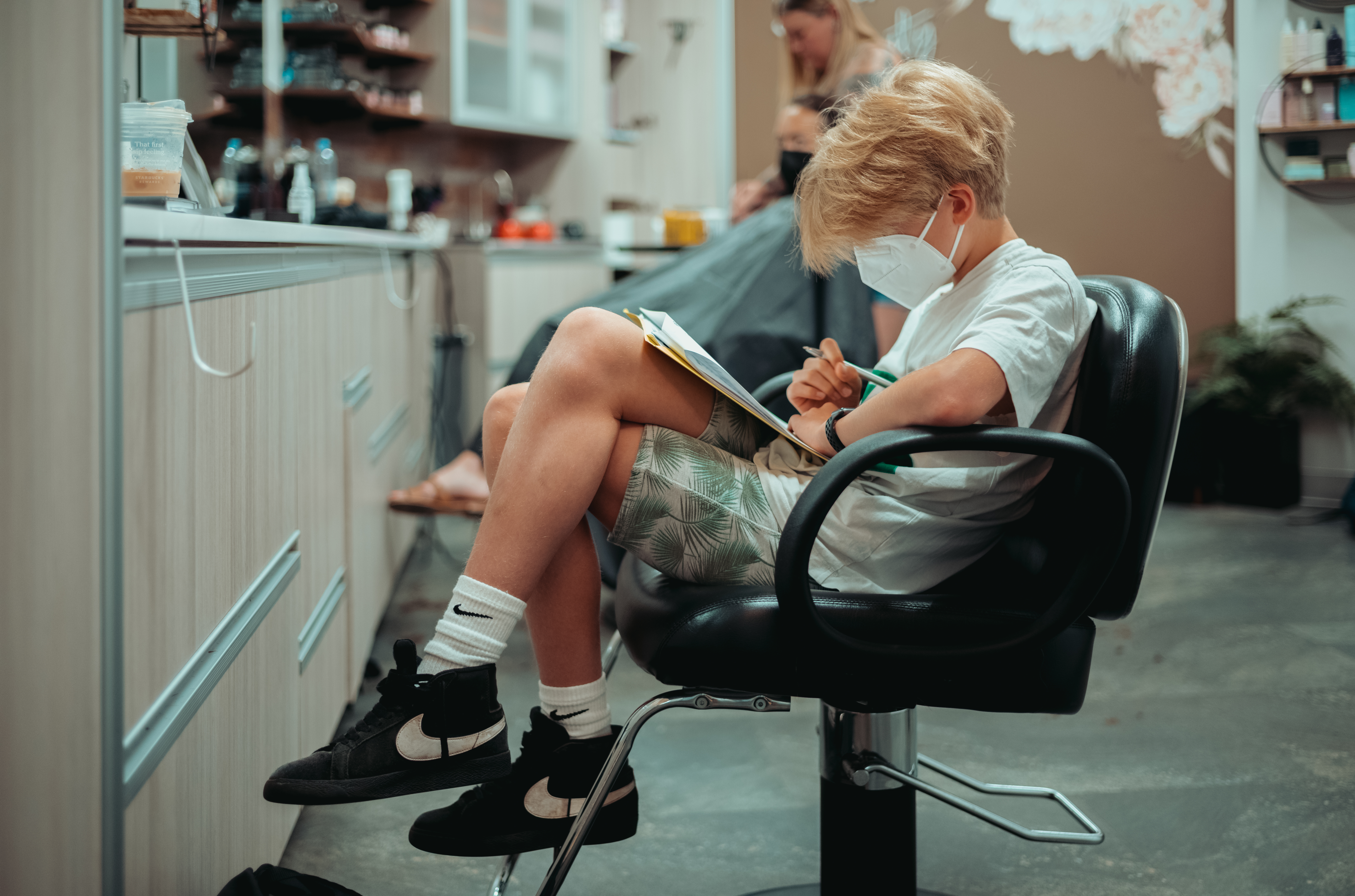 A boy wearing a mask sitting in a chair at the hairdresser.