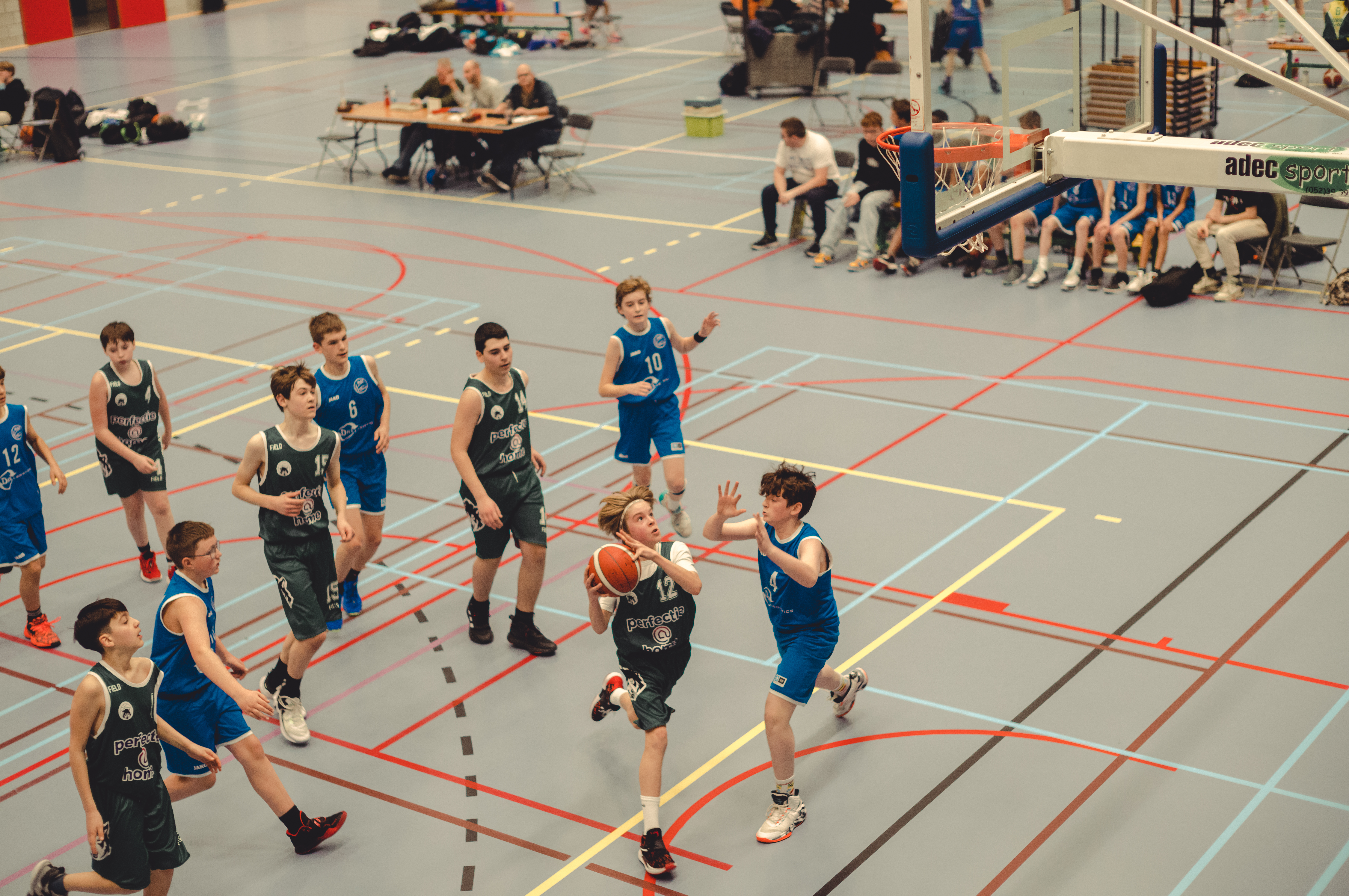 A teenage boy with a basketball runs towards the basket, while players from the other team try to catch him. He started his layup before they could reach him.