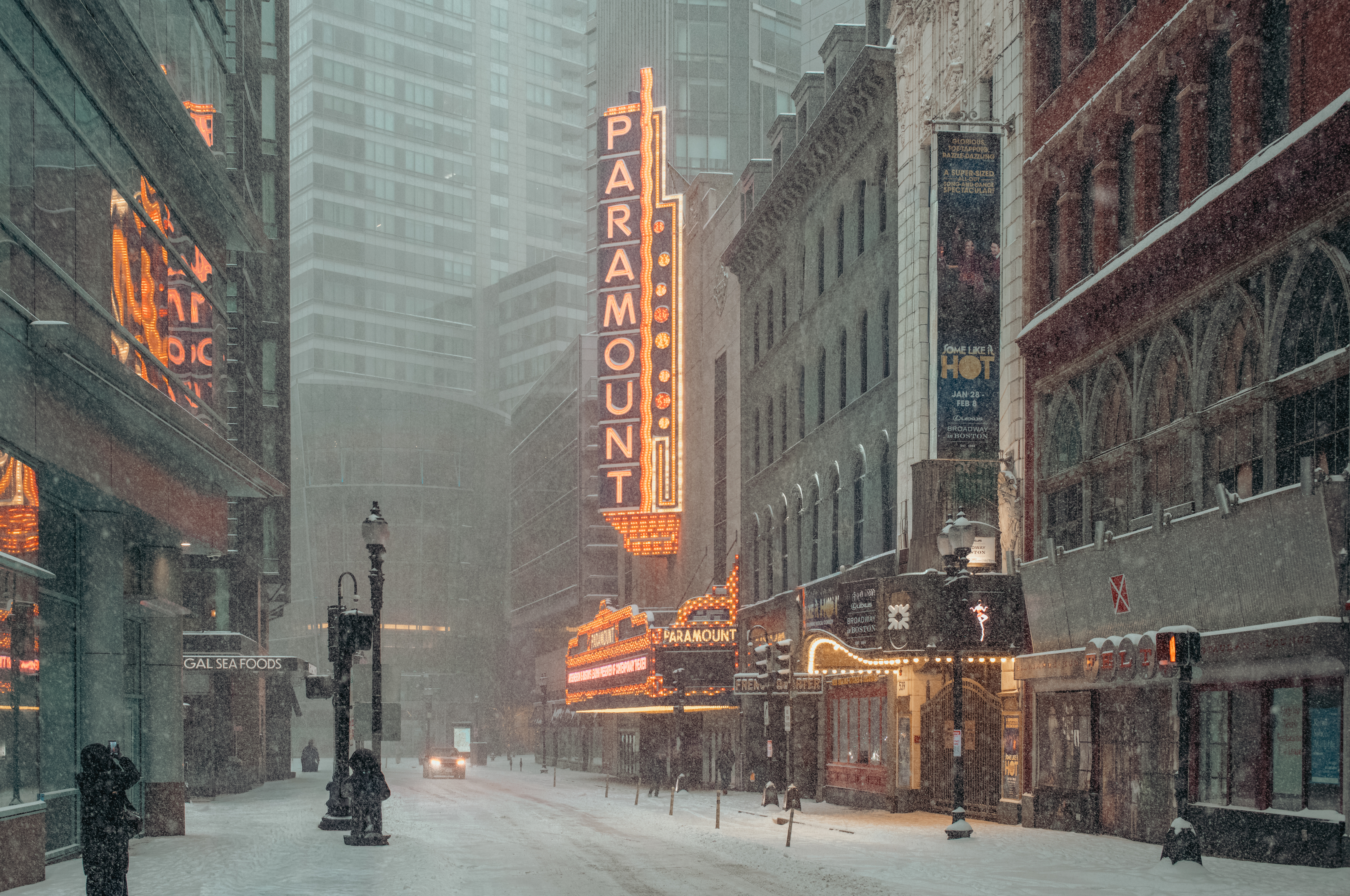 An empty street in downtown Boston during a snowstorm, lit by the orange Paramount Theatre sign.