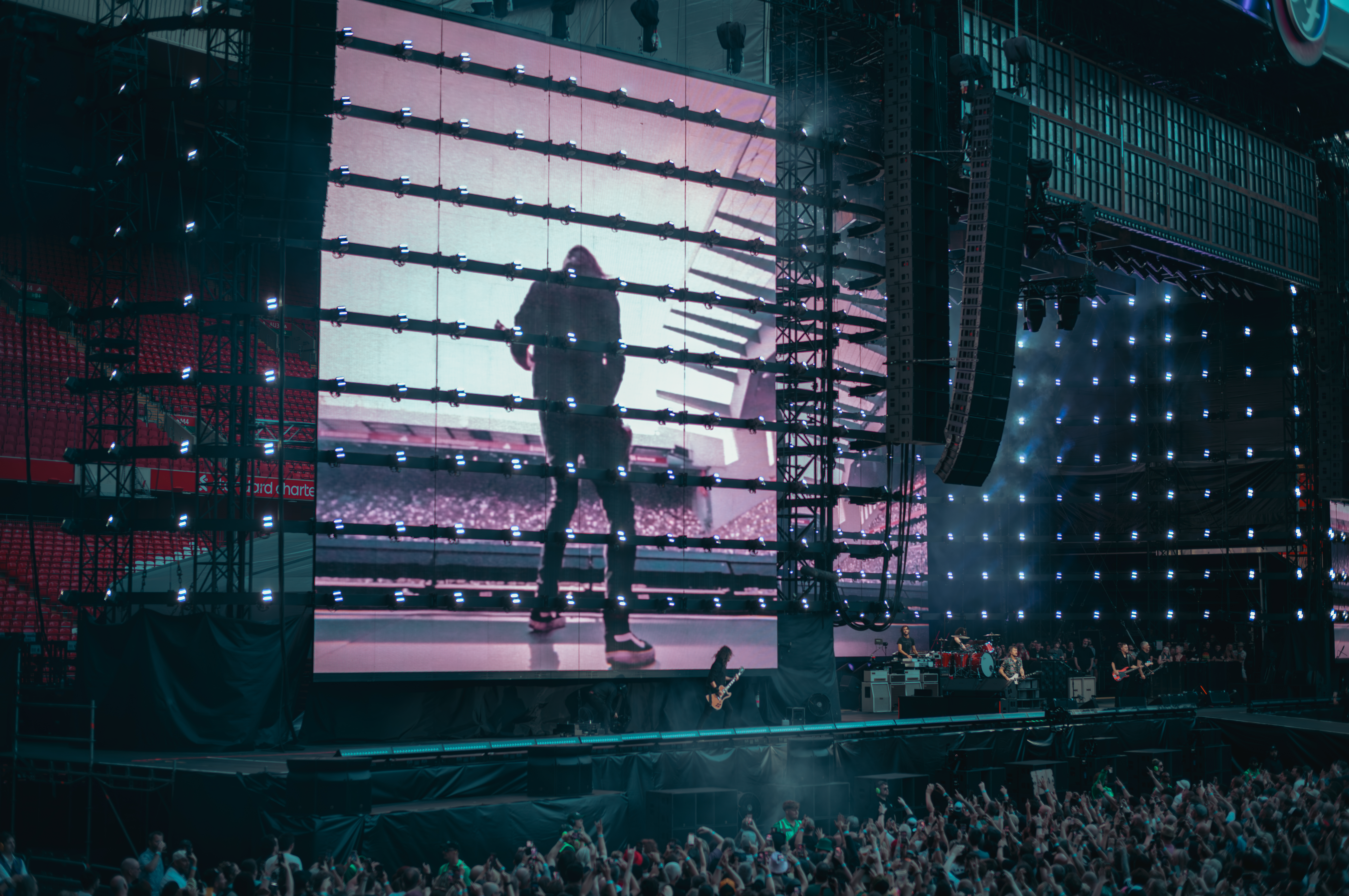 The Foo Fighters perform on a large stadium stage in Liverpool, UK, with a giant video screen showing Dave Grohl.