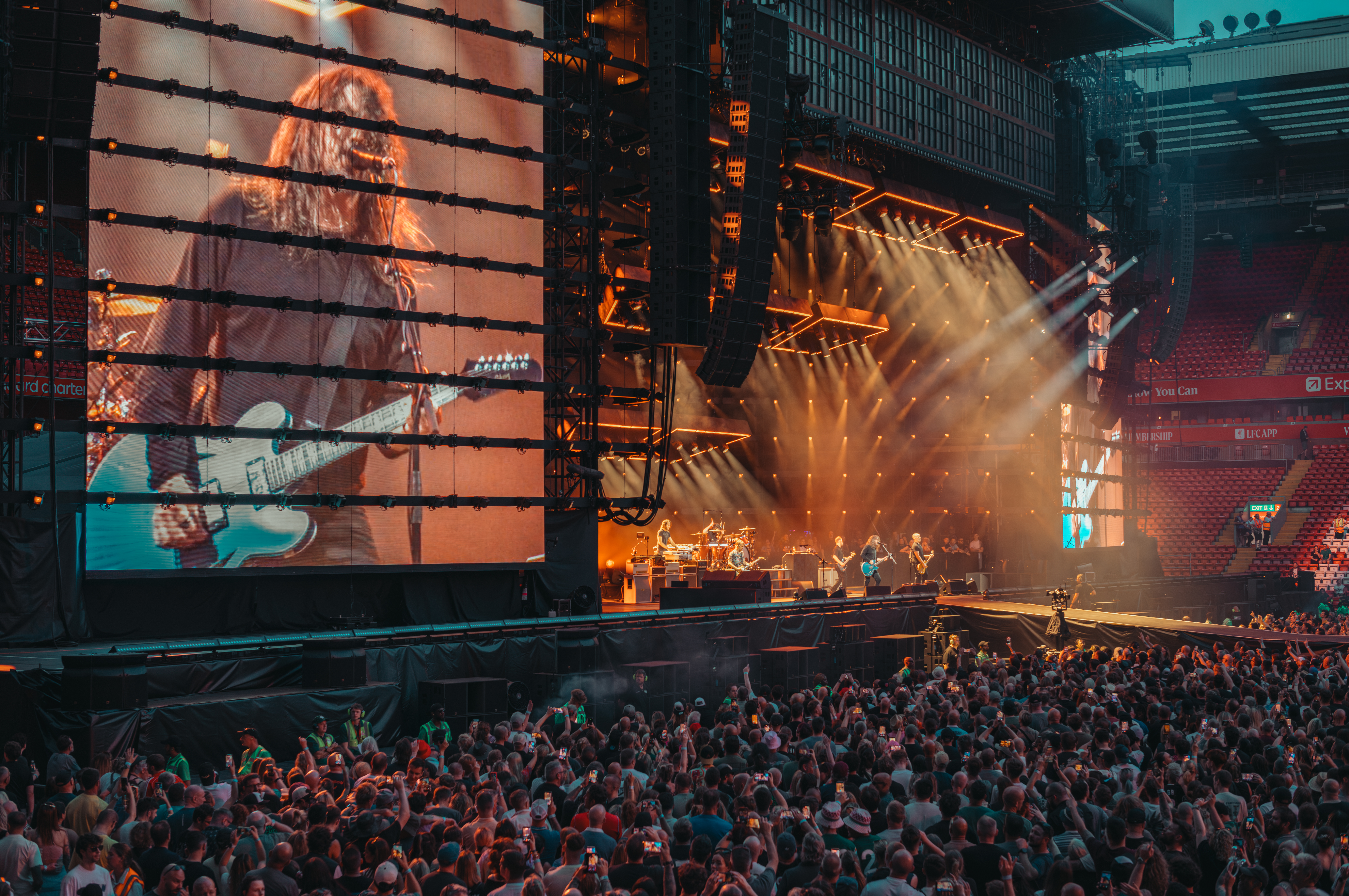 The Foo Fighters perform on a large stadium stage in Liverpool, UK, with a giant video screen showing Dave Grohl.