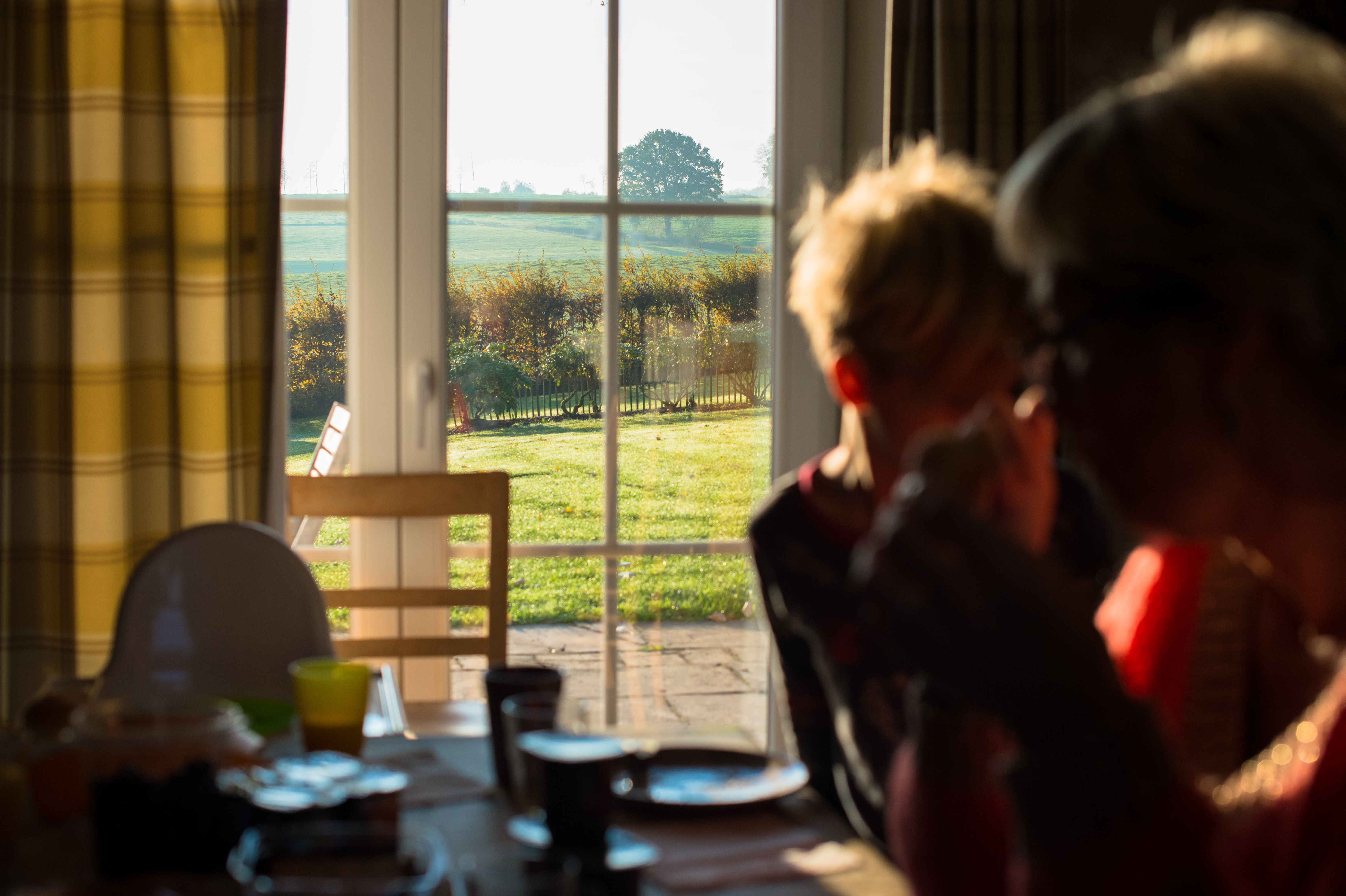 Two people have breakfast at a table near a window with a view of a sunny countryside.