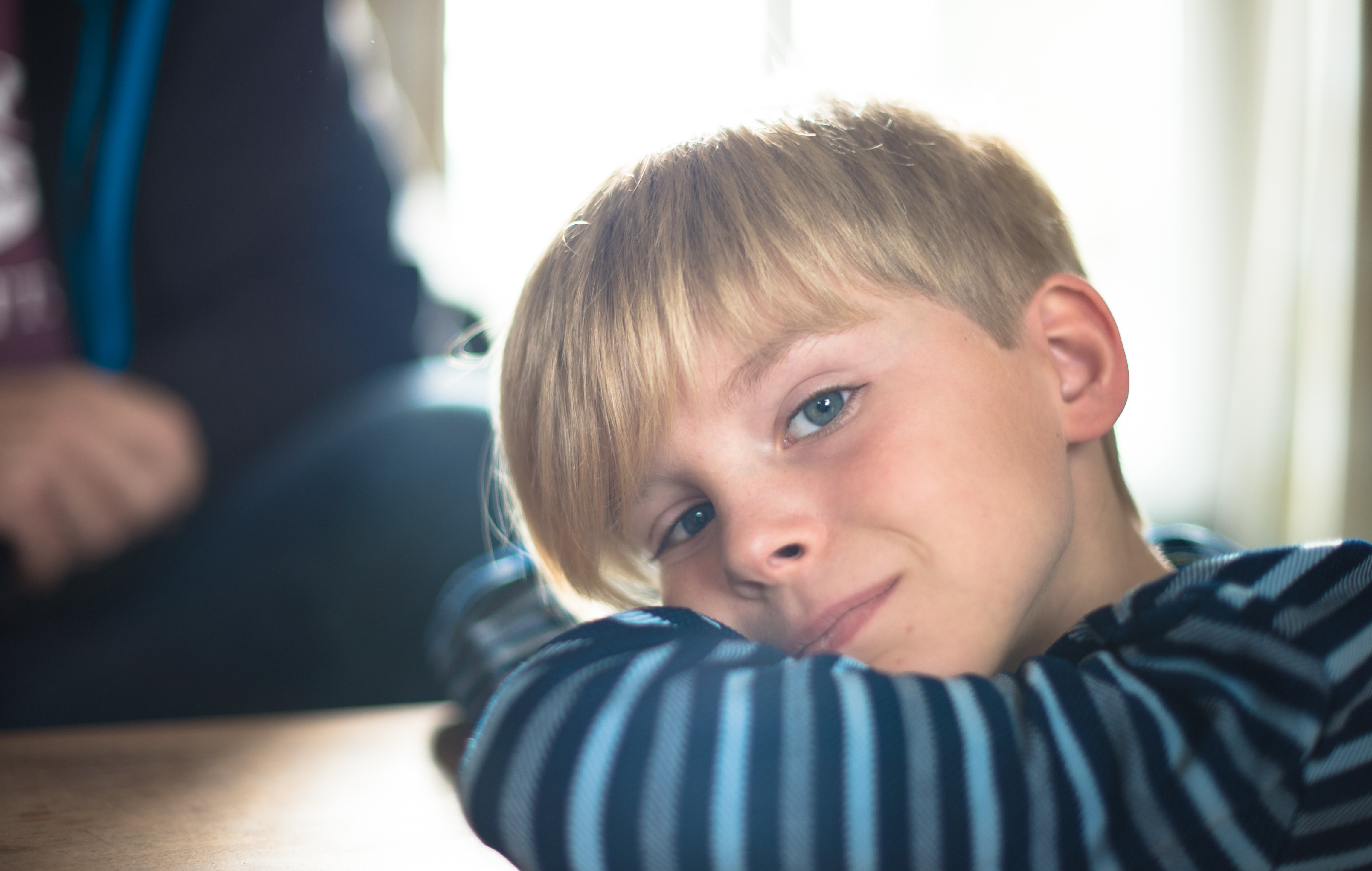 A young boy with blond hair rests his head on his arms, gazing softly at the camera.