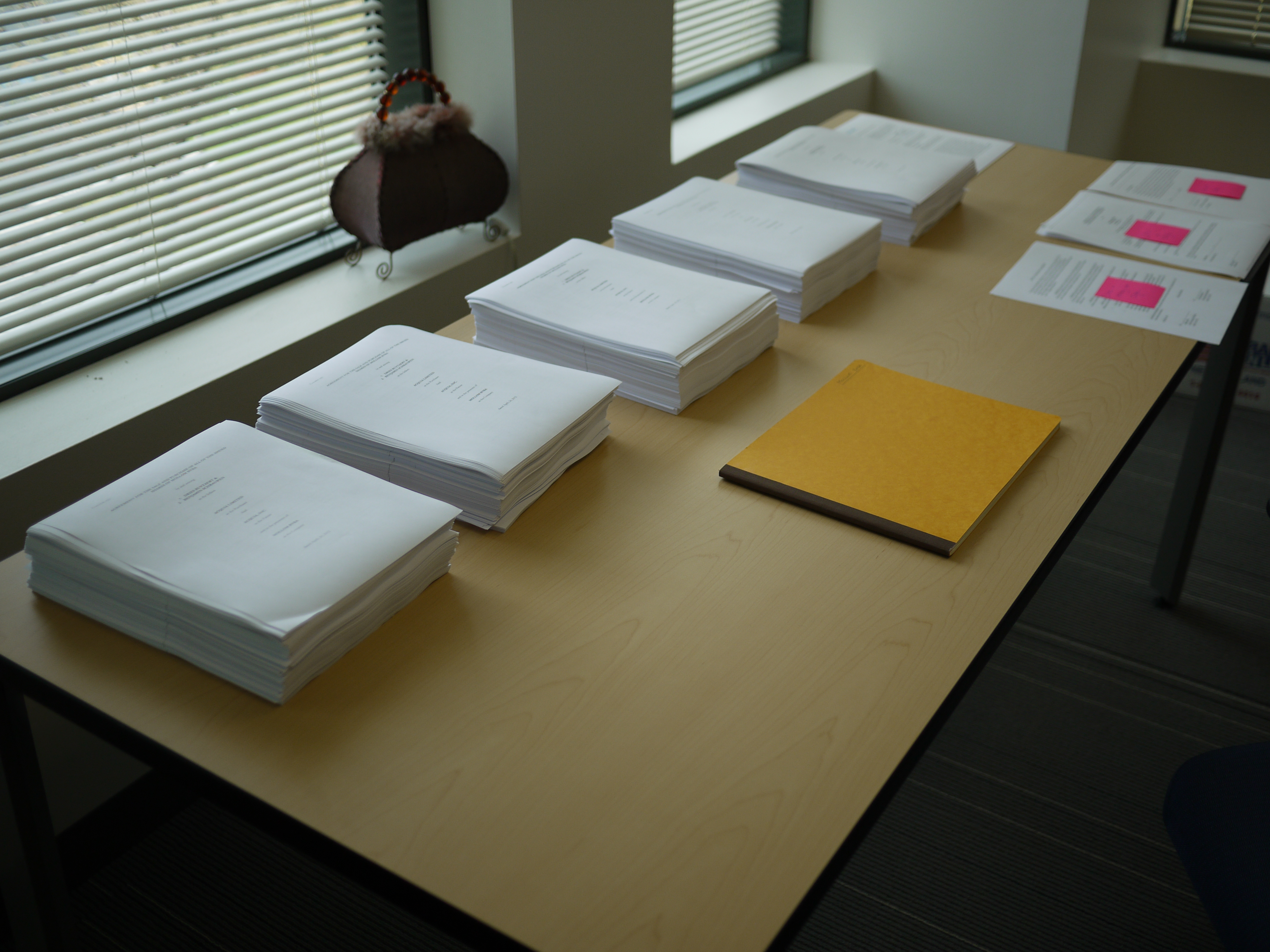 Stacks of printed documents and a folder are neatly arranged on a table in an office setting.