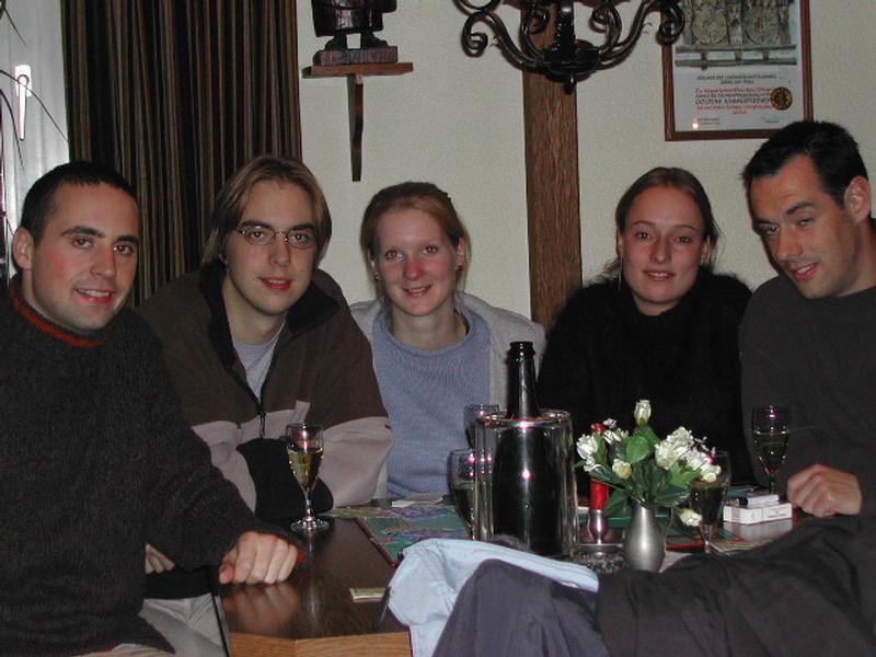 Five people sitting at a table with drinks, smiling and posing for the camera in a cozy indoor setting.
