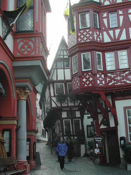 A person in a blue jacket walks on a cobblestone street surrounded by historic half-timbered buildings.