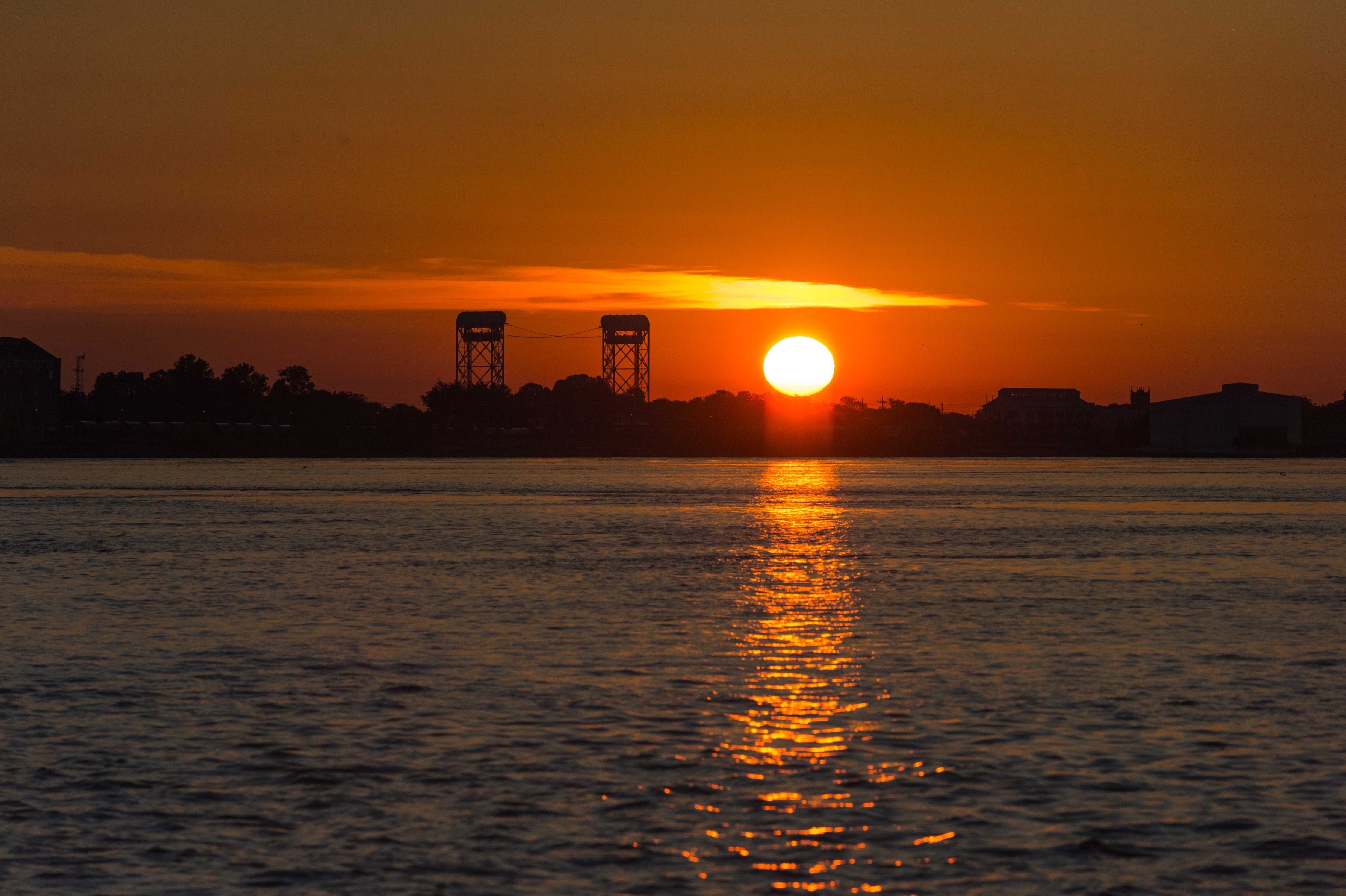The sun rises over the water, casting a bright reflection.