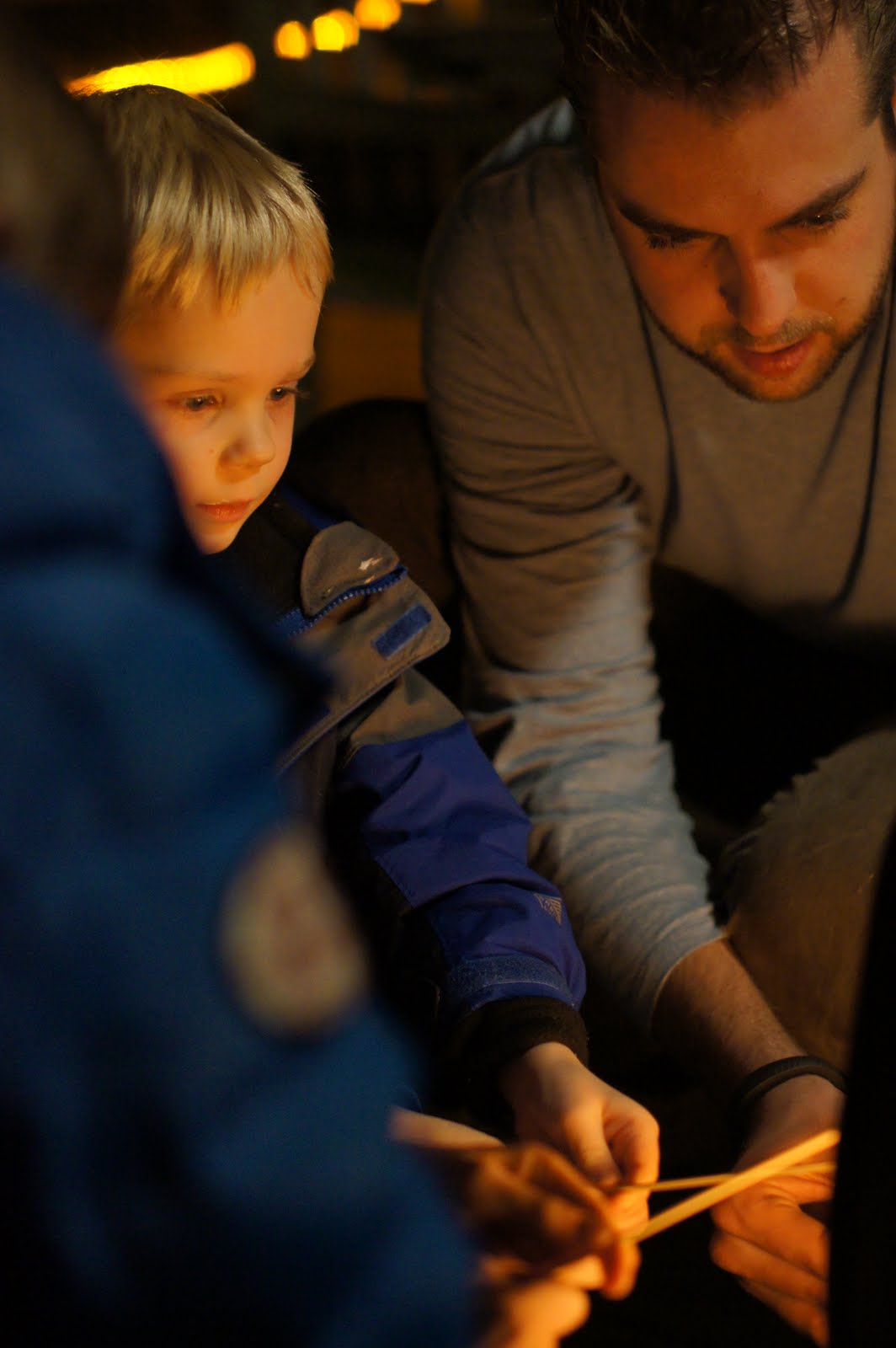 A child and an adult light candles together in a dimly lit setting, focusing on the flames.