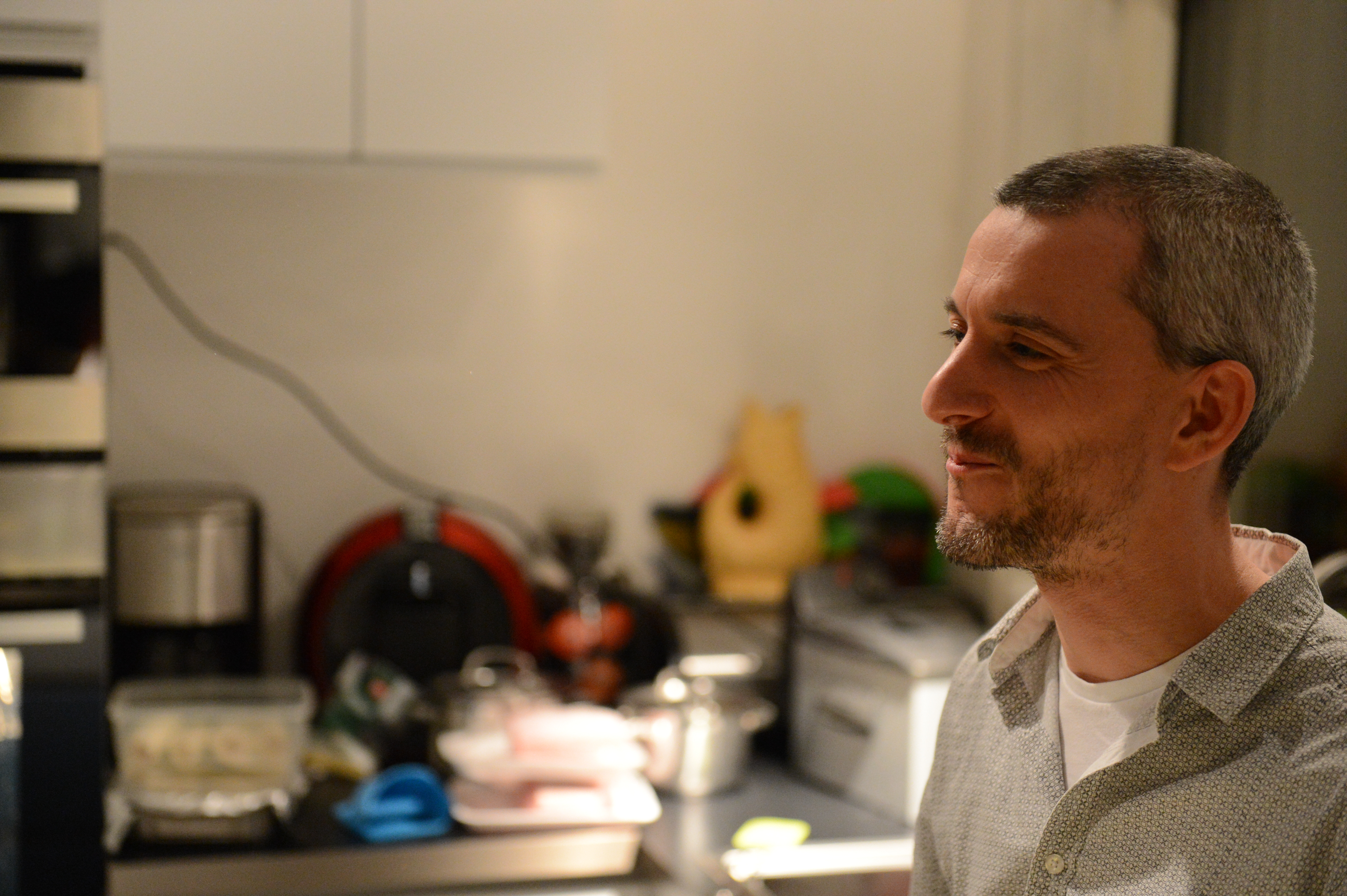 A man with short hair and a beard smiles while standing in a kitchen during a New Year's Eve party.