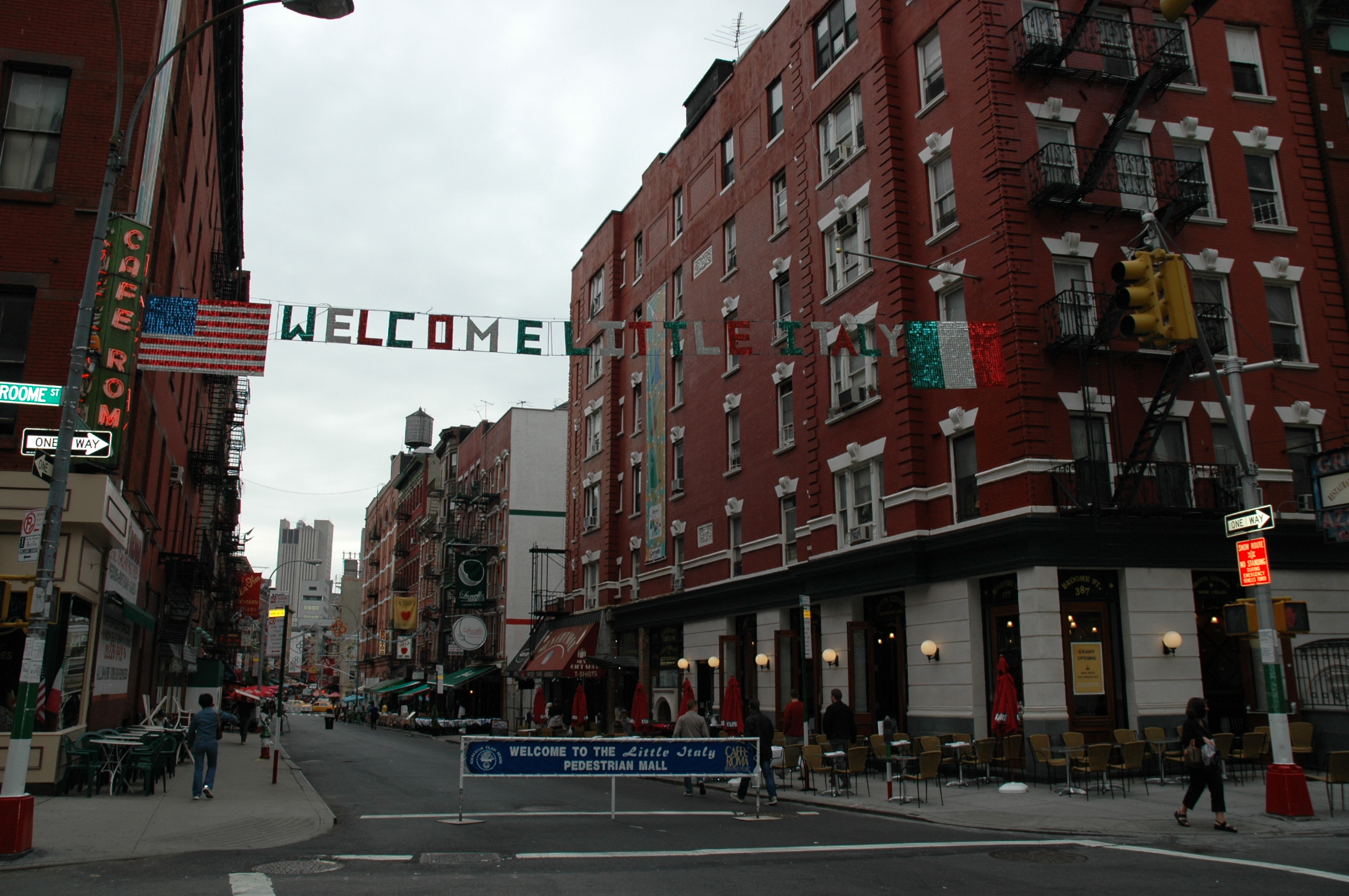 A street in Little Italy with a "Welcome to Little Italy" banner hanging between red brick buildings.