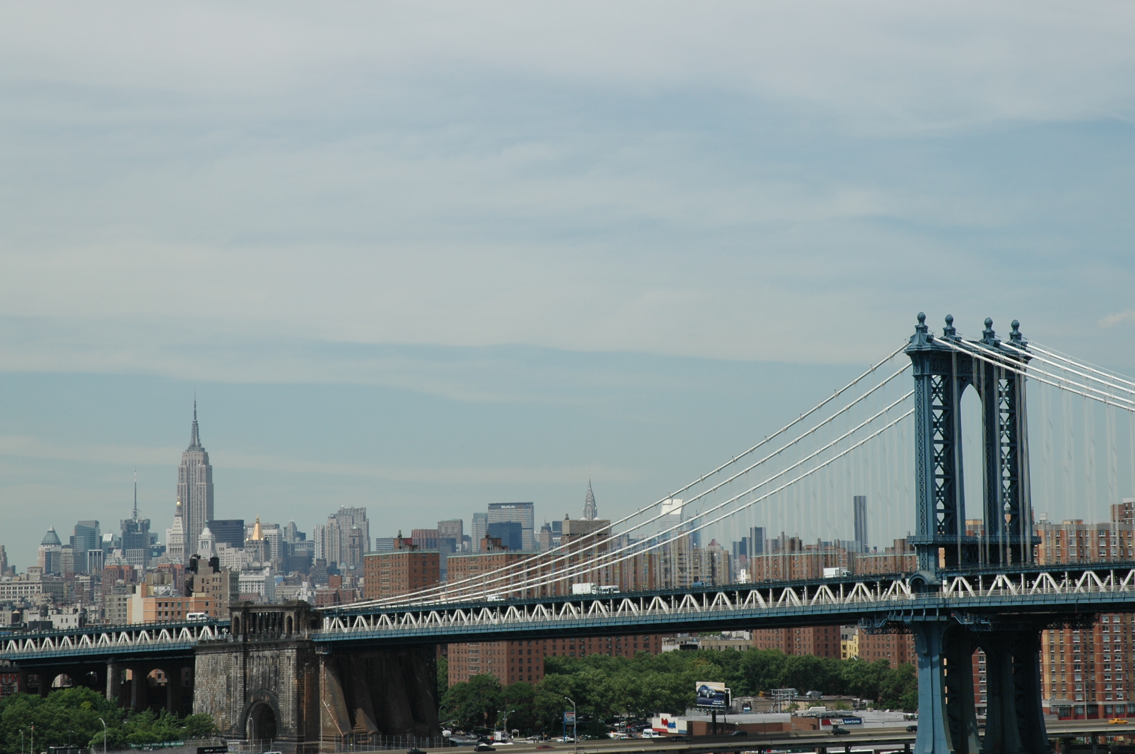 The Manhattan Bridge with the New York City skyline, including the Empire State Building, in the background.