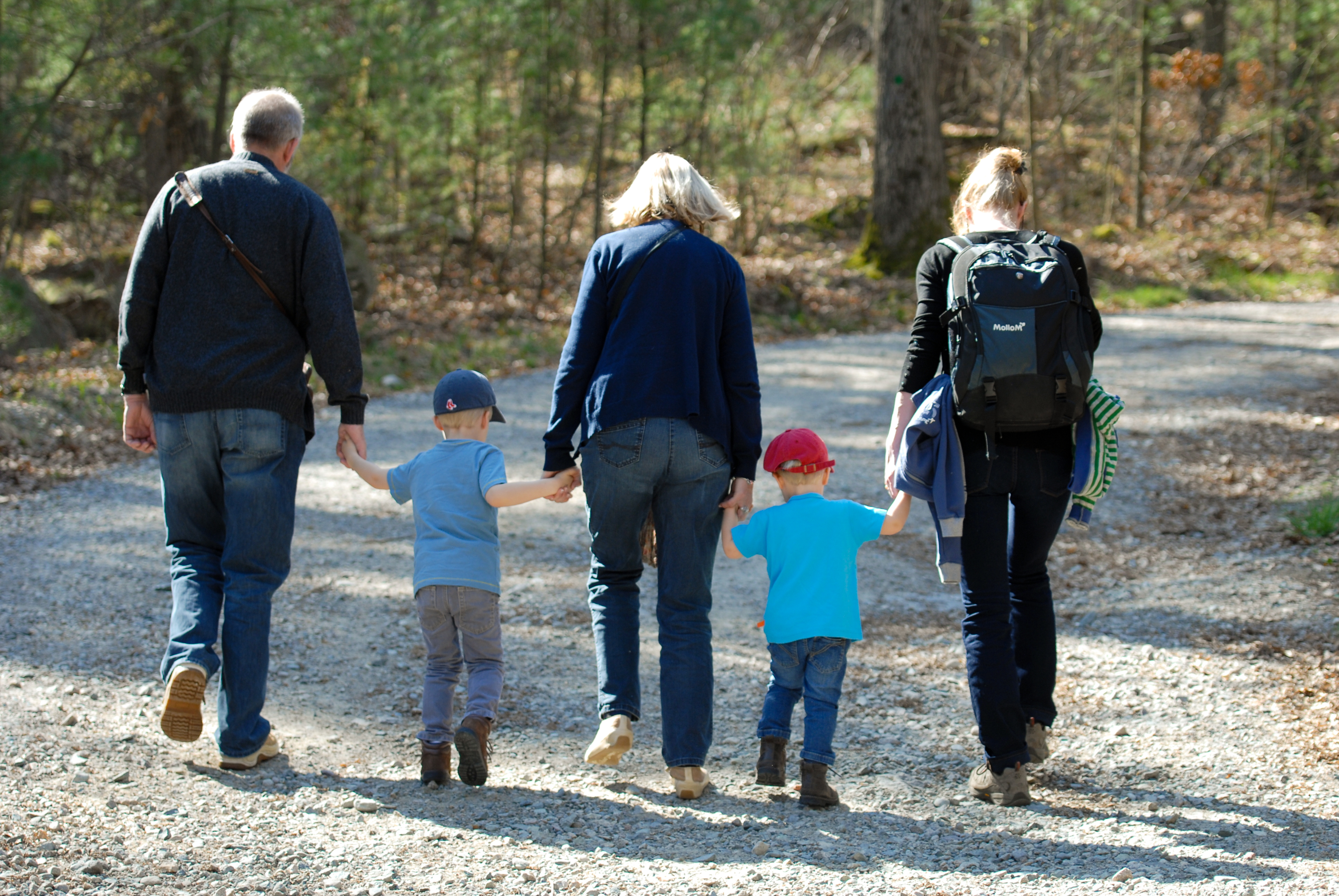 Two adults and two children walk hand in hand on a gravel trail surrounded by trees.