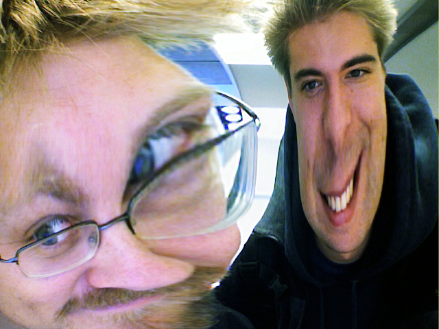 Two people with digitally distorted faces, one wearing glasses and the other grinning widely.