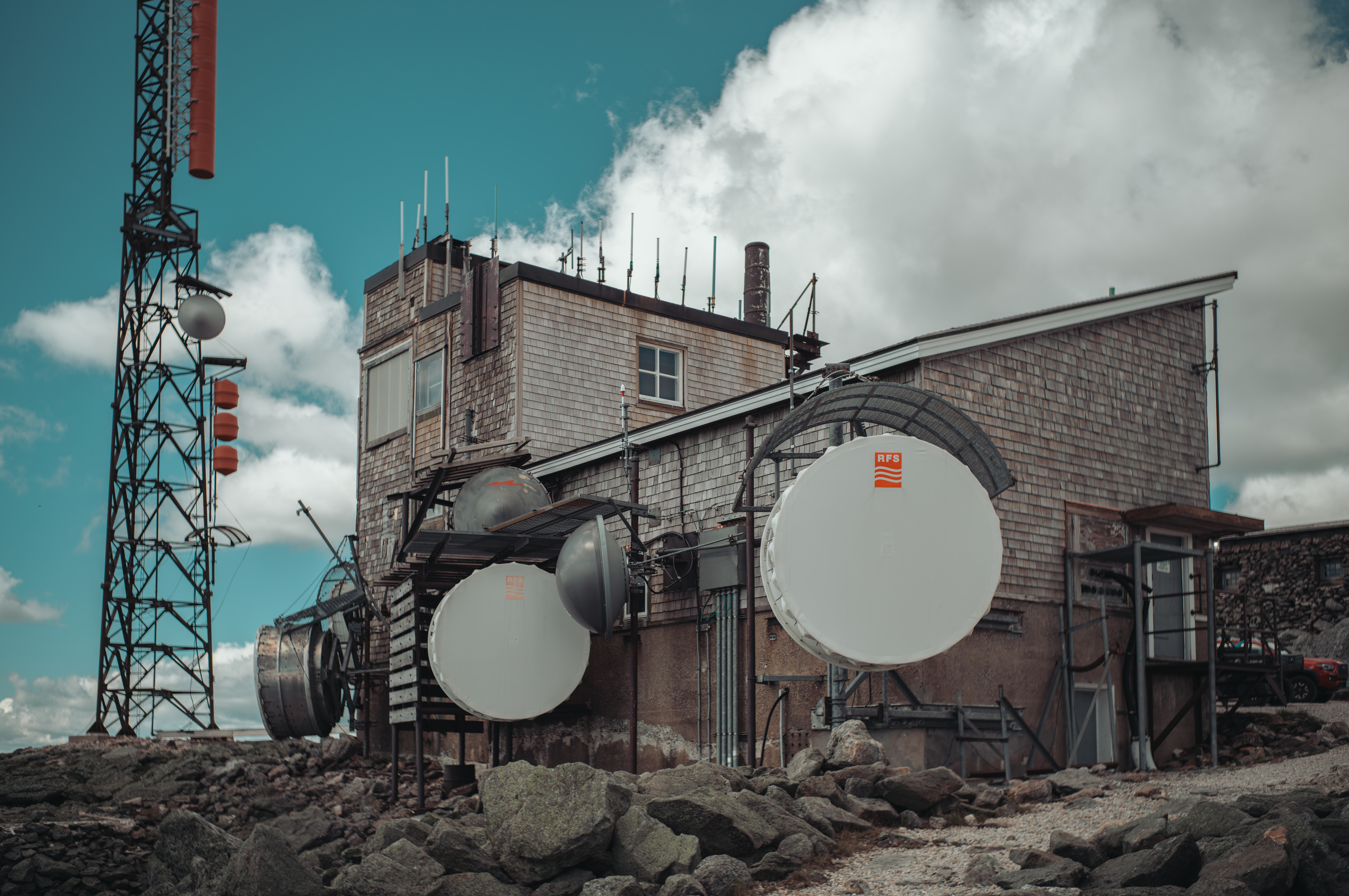 A weather station building with large satellite dishes and antenna at the top of a rocky summit.