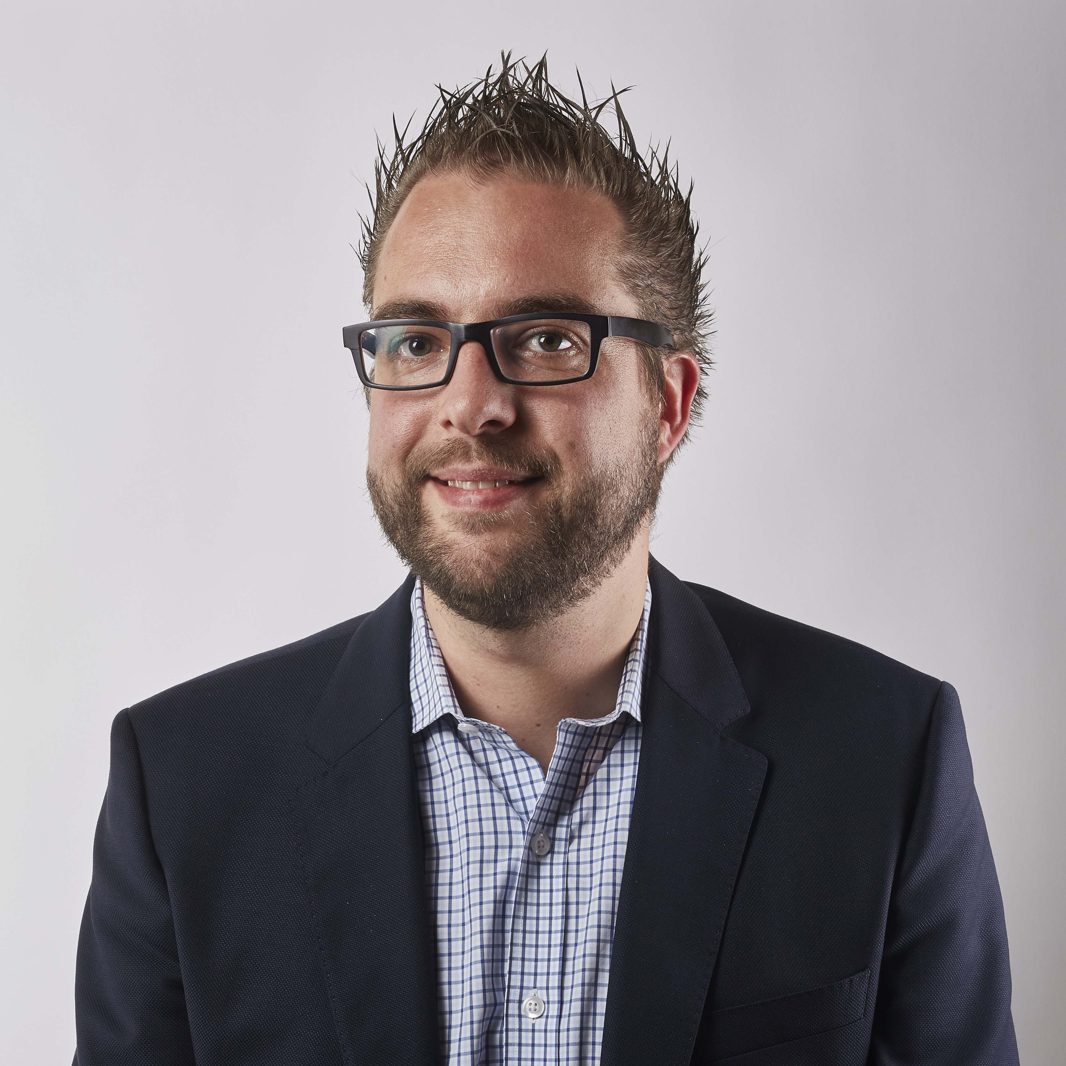A man wearing glasses and a suit jacket smiles in a professional headshot against a plain background.