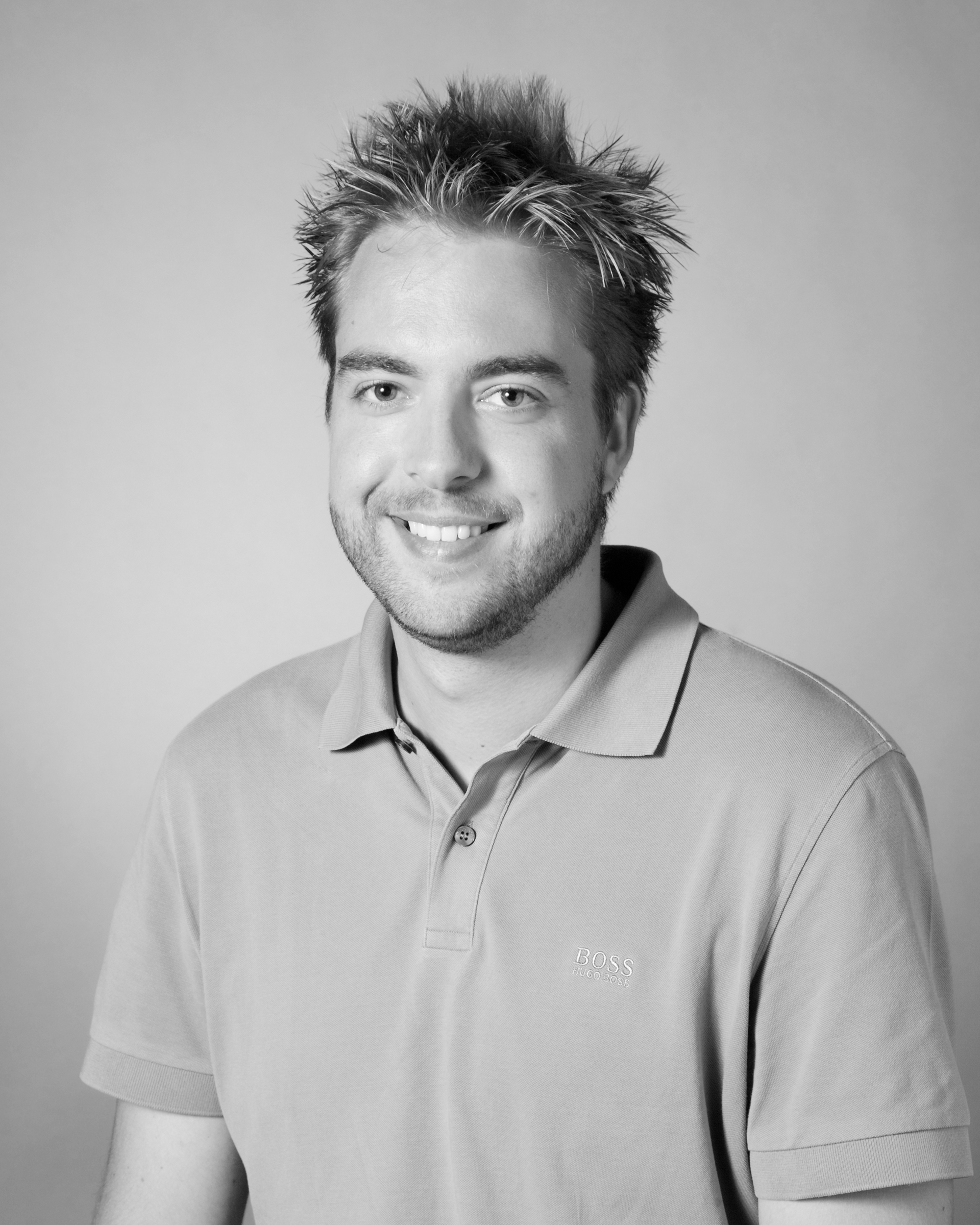 Black and white portrait of a smiling man with short, spiky hair, wearing a collared polo shirt.