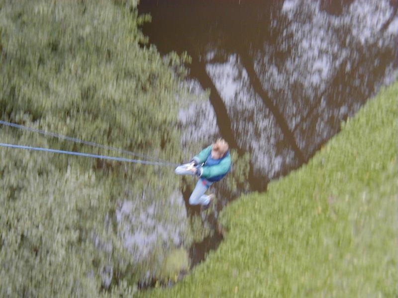 A person in a blue jacket swings on a rope over a body of water during a bungee jump.