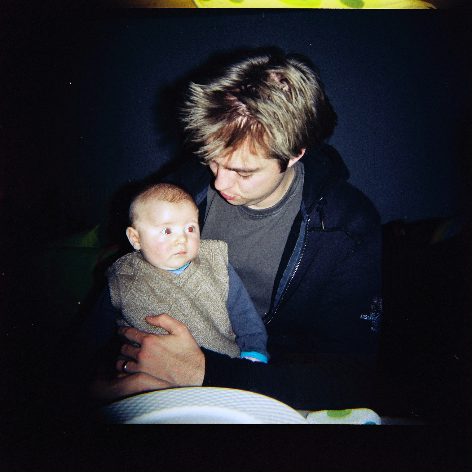 A man holds a baby in his arms, looking down while the baby gazes off to the side.