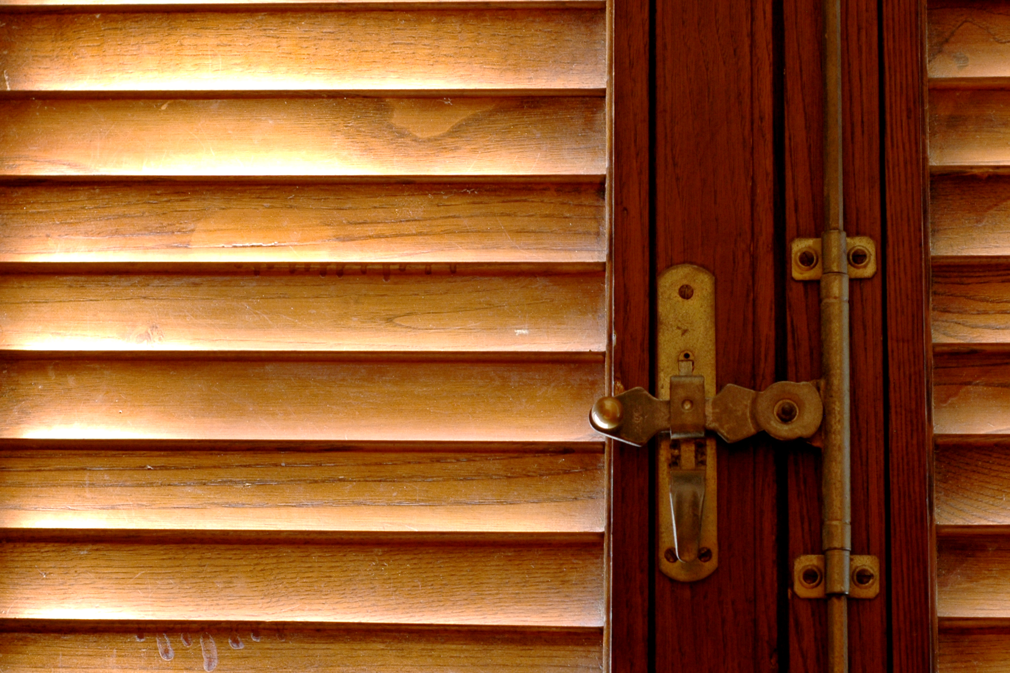 Sunlight filters through wooden shutters, casting a warm glow on a closed window with a brass latch.