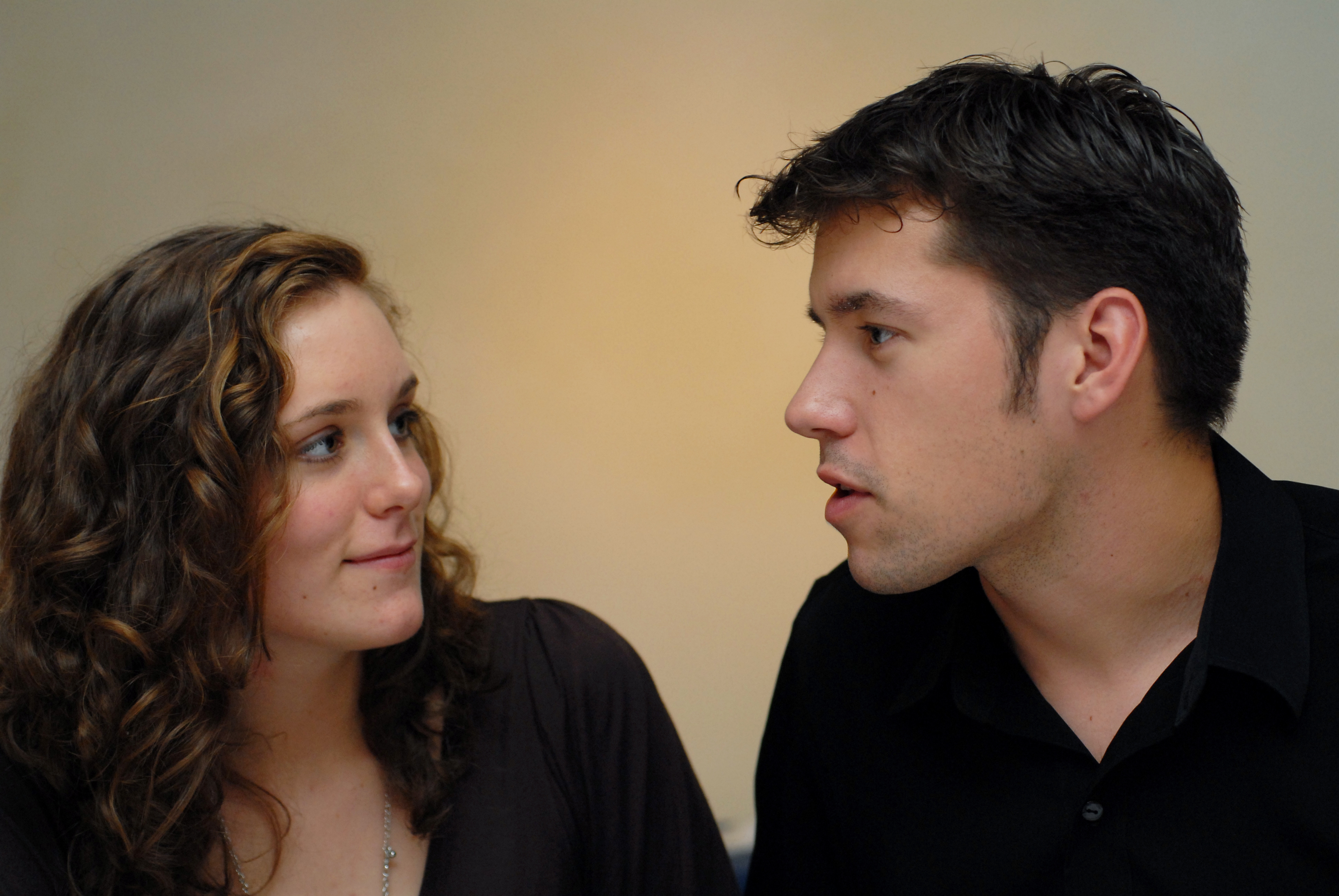 A man in a black shirt speaks while a woman with curly hair listens and looks at him.