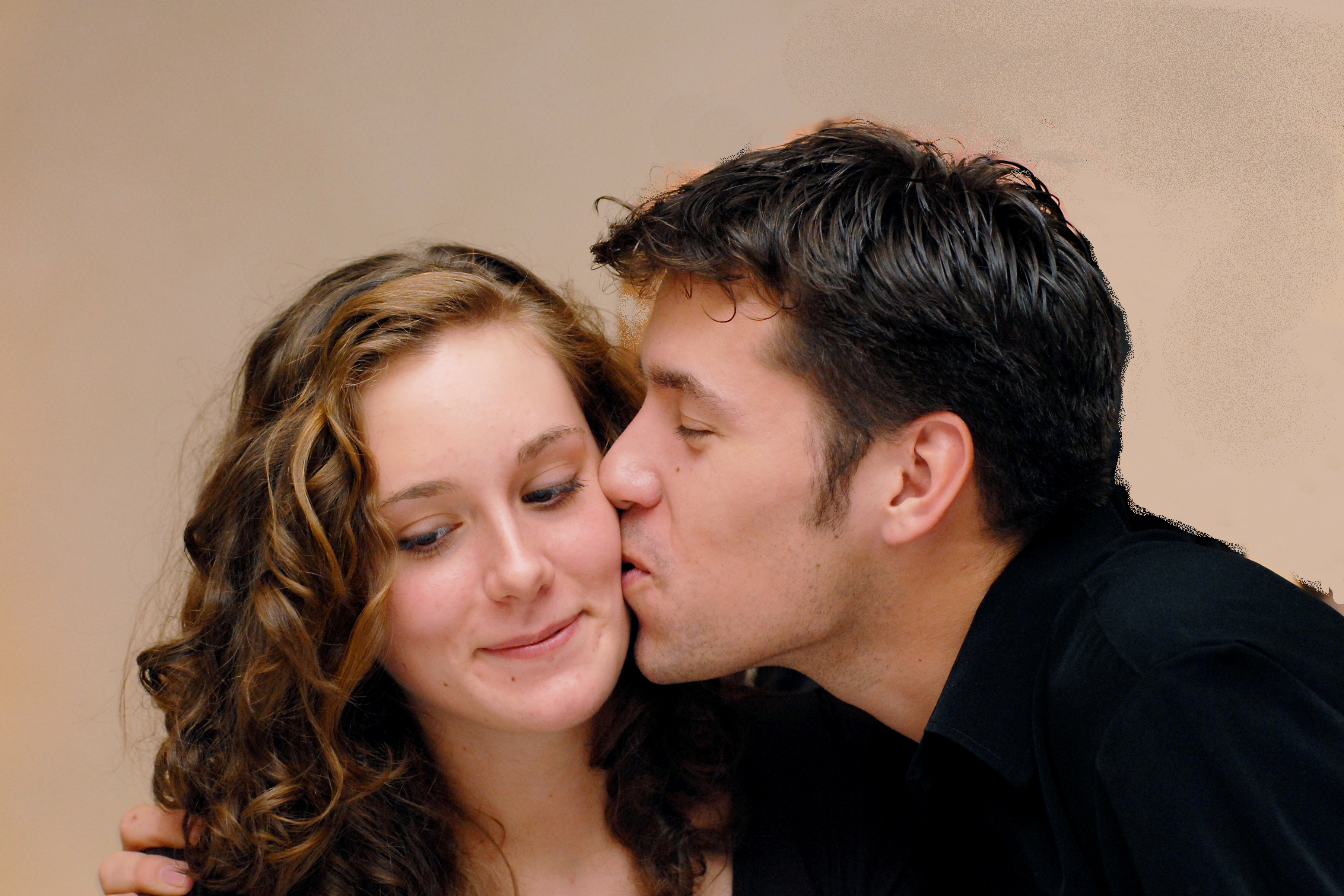 A man in a black shirt kisses a smiling woman on the cheek.