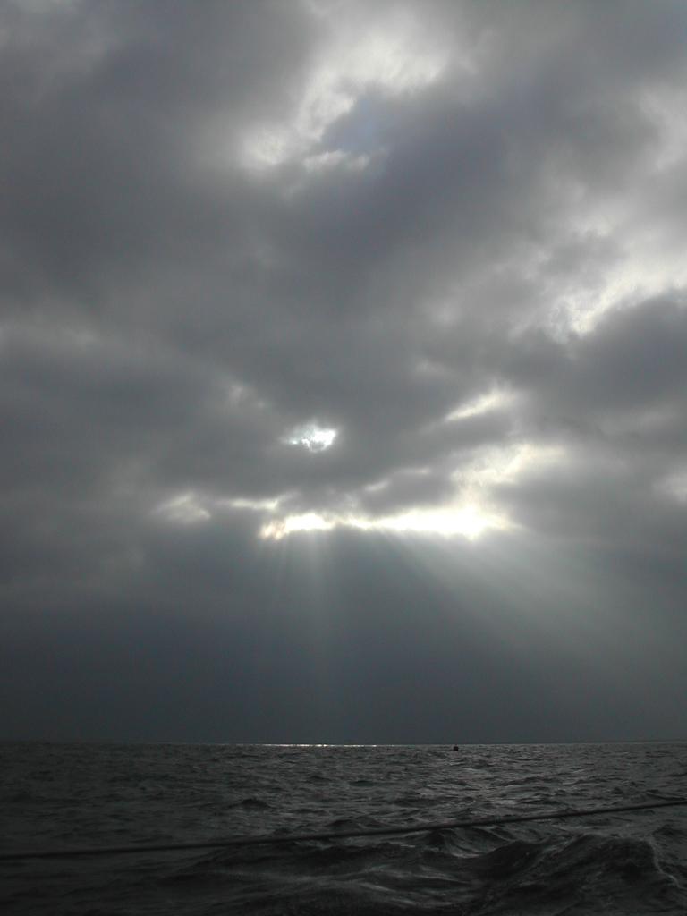 Dark clouds cover the sky as sunlight breaks through, casting rays over the ocean's surface.