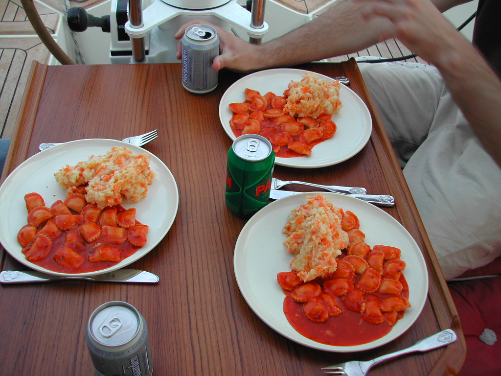 Three plates of ravioli with sauce and rice sit on a wooden table, with drinks and a person's arm visible.