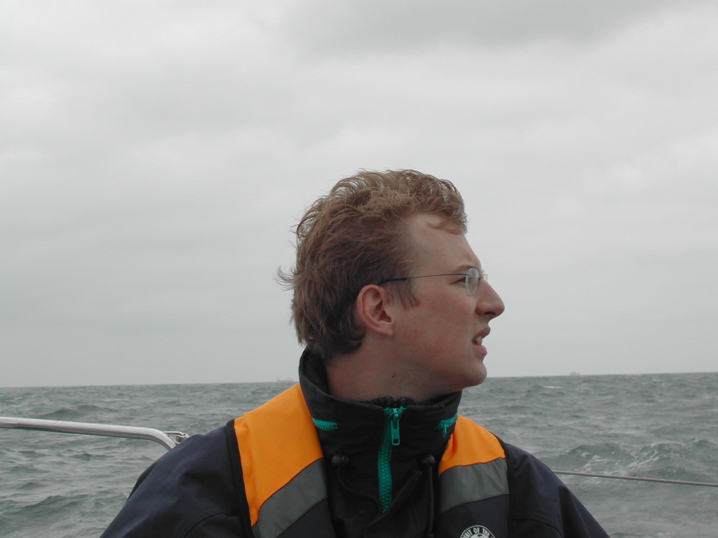 A person wearing a life jacket looks to the side while on a boat in the open water.