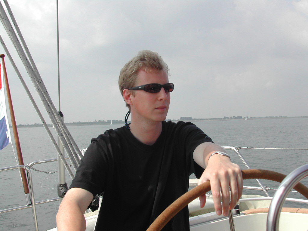 A person wearing sunglasses and a black shirt steers a boat on the water under a cloudy sky.