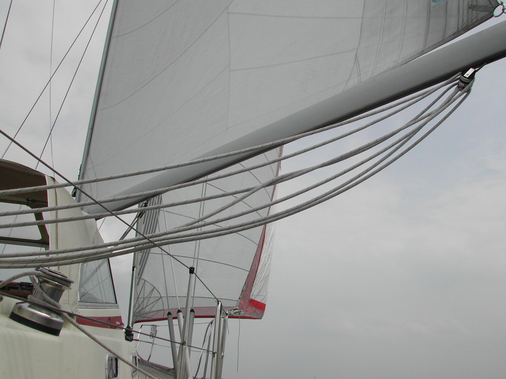 Close-up of a sailboat's rigging and sails, with ropes and winches visible against a cloudy sky.